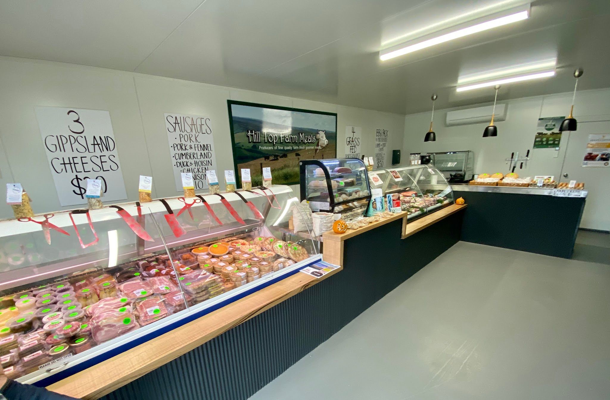 Hill Top Farm Meats shop interior showing full butcher counter, display cases, pendant lights and branded wall art