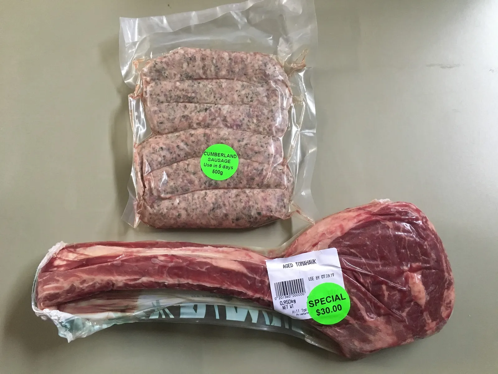 Cumberland sausage ring and aged tomahawk steak with price labels on plain surface