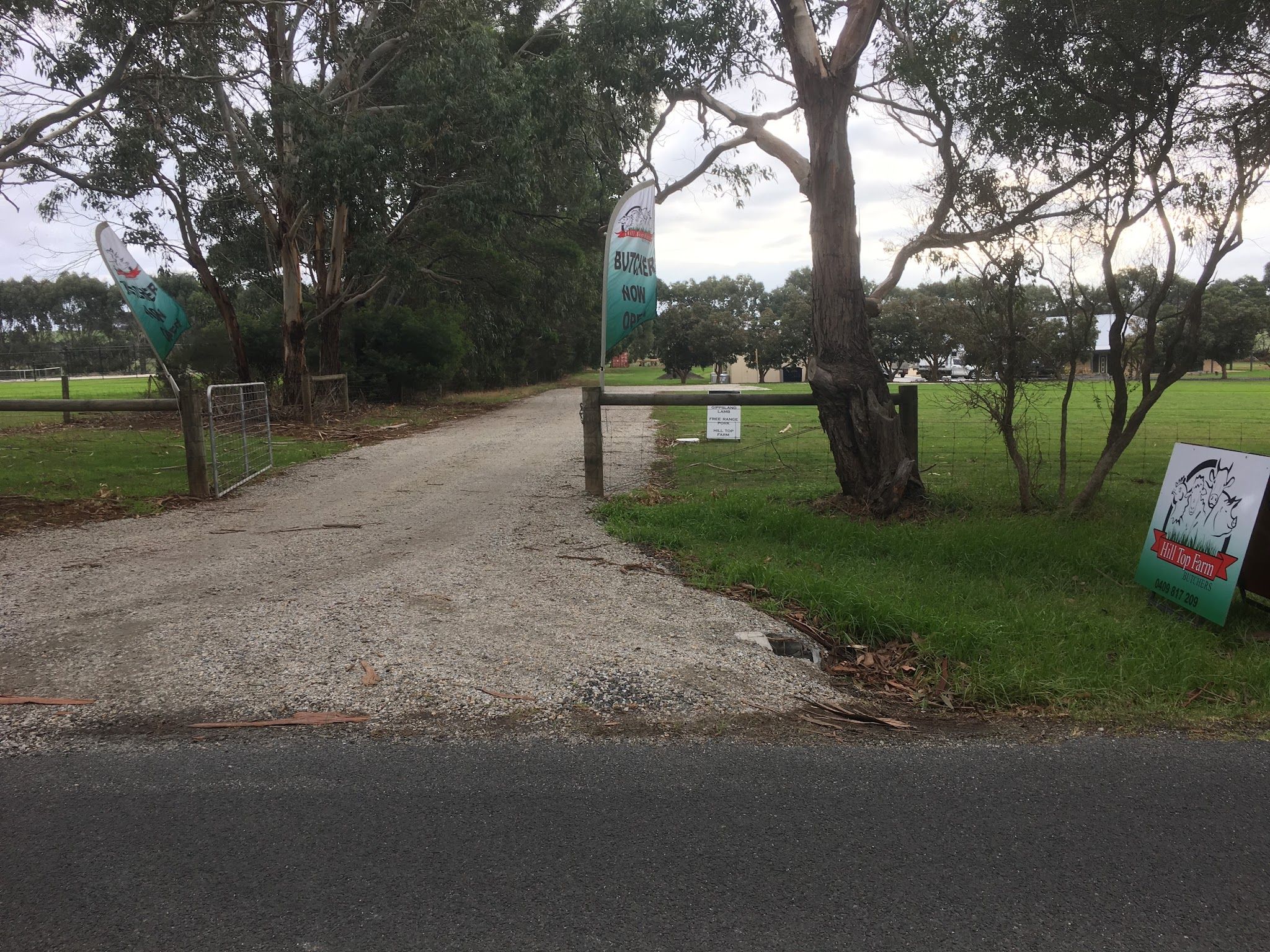 Gravel driveway entrance to Hill Top Farm property with timber gate and branded sign among native trees